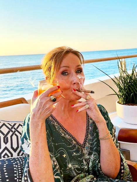 J.K. Rowling smoking a cigar and drinking while on a boat.