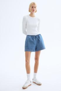 Woman wearing white long-sleeve shirt and denim shorts.