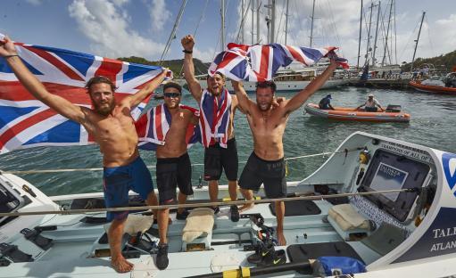 Four British rowers celebrating their victory in the Talisker Whisky Atlantic Challenge, holding Union Jack flags.