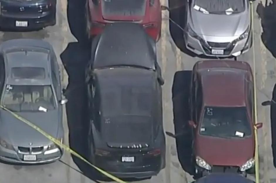 Aerial view of several cars in a tow yard with yellow crime scene tape across a black Tesla and a gray BMW.