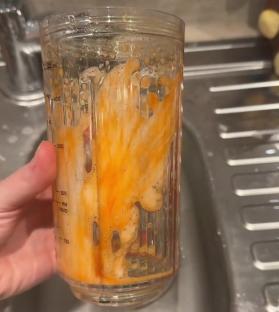 A hand holding a stained blender cup in a sink.