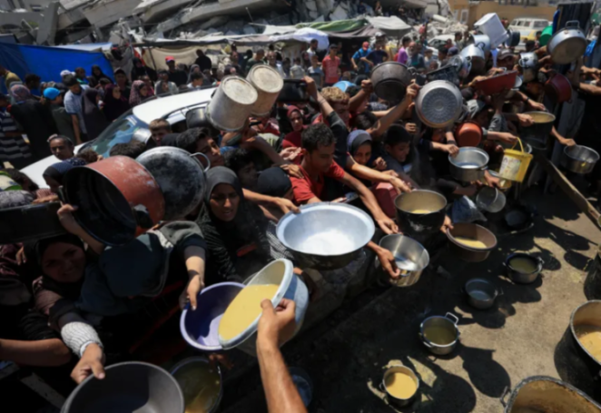 People in a crowded area receiving food rations from large pots and bowls into their own containers.
