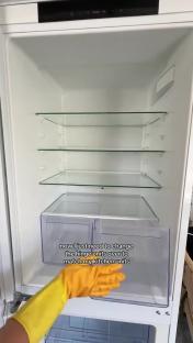 Empty fridge interior with a person in yellow gloves adjusting a crisper drawer.