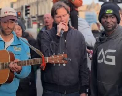 Street performer singing and playing guitar with a crowd watching.