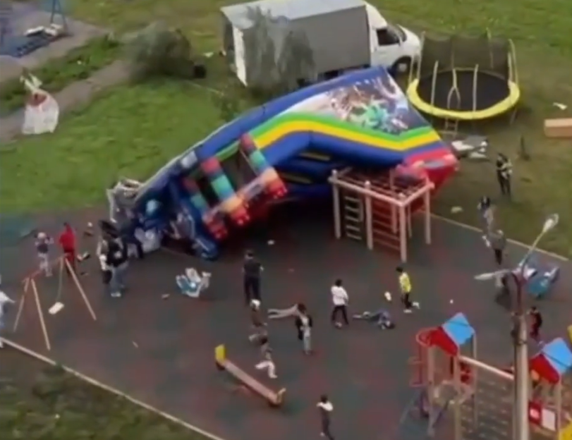 Inflatable playground equipment overturned in a playground with children and adults around.