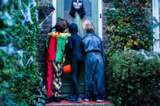 Three children in Halloween costumes trick-or-treating at a decorated house.