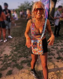 Woman at an outdoor festival wearing a colorful top, black shorts, fishnet stockings, and Doc Martens.