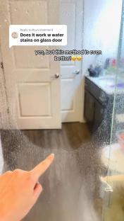 Hand pointing at soap scum and limescale on a shower door.