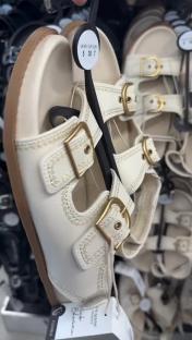 Close-up of cream-colored children's sandals with gold buckles.