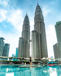 Woman in a swimsuit standing in a hotel pool with the Petronas Towers in the background.