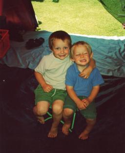 Two young boys sitting together inside a tent.