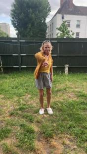 Woman in a mustard cardigan and striped skirt dancing in a backyard.