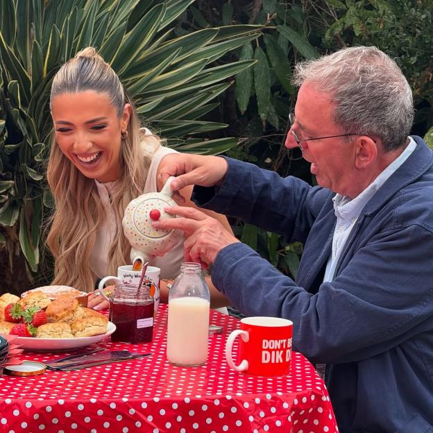 Two people at an outdoor table, pouring tea and enjoying scones and strawberries.