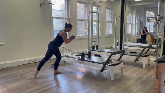 Woman doing Pilates leg exercises on reformer.