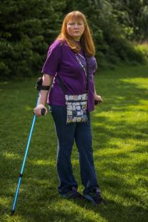 Woman with a crutch standing in a grassy area.