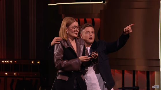 Screenshot of two people on a stage, one pointing.