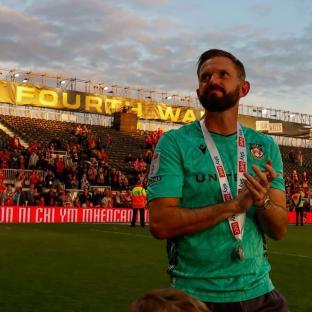 Man in teal soccer uniform with medal, applauding in stadium.