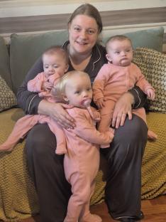 A mother holding her three babies, including a set of twins.