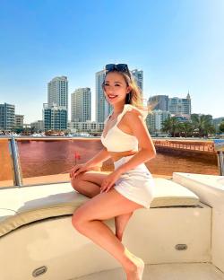 Woman in white outfit sitting on a boat, city skyline in the background.
