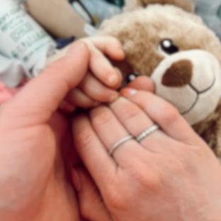 Close-up of two hands holding a baby's hand, with a teddy bear in the background.