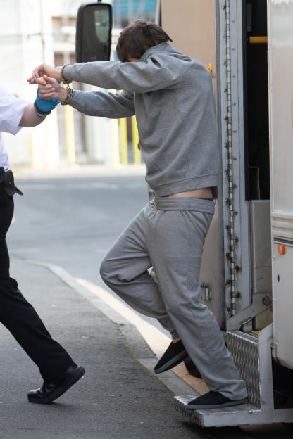 Matthew Battenbough, in handcuffs and a grey tracksuit, being led into a vehicle.