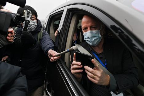 A man in a car wearing a mask speaks to reporters.