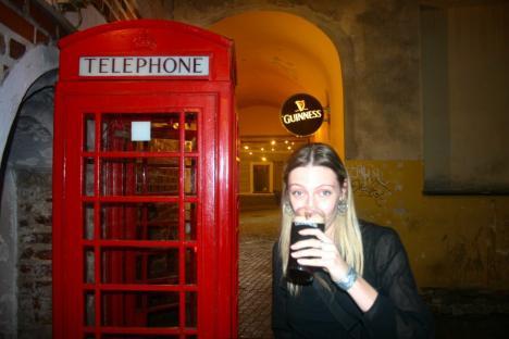 Woman drinking Guinness by a red telephone booth.