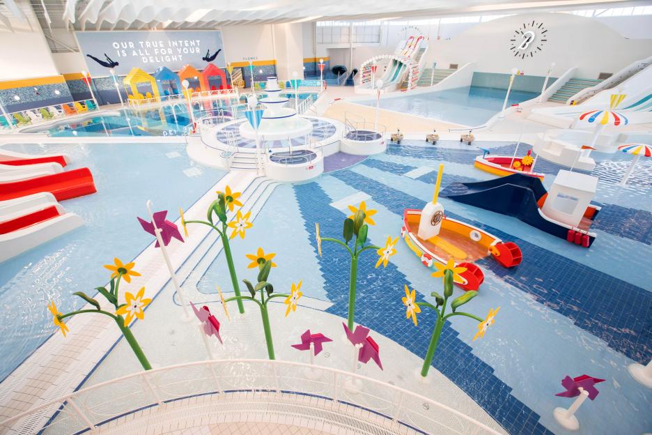 Indoor swimming pool with water slides and play features.