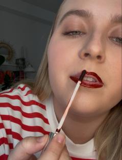 Person applying dark red lip gloss.