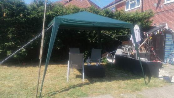 Green gazebo in a backyard with two chairs and a small table.