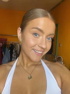 Woman wearing a white top and gold necklace.