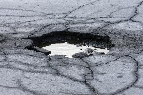 Pothole in cracked asphalt road filled with water.