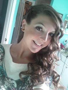 Woman in denim vest giving peace sign; she is wearing large gold hoop earrings and a gold necklace.