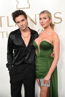 Liam Payne in a black satin shirt and Kate Cassidy in a green strapless dress attend an event.