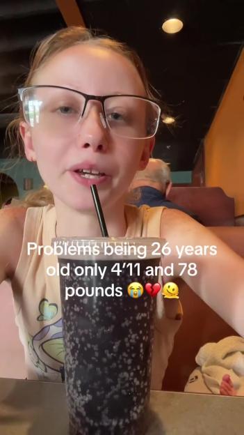 A young woman drinks from a large soda while talking about being 26 years old, 4'11", and 78 pounds.