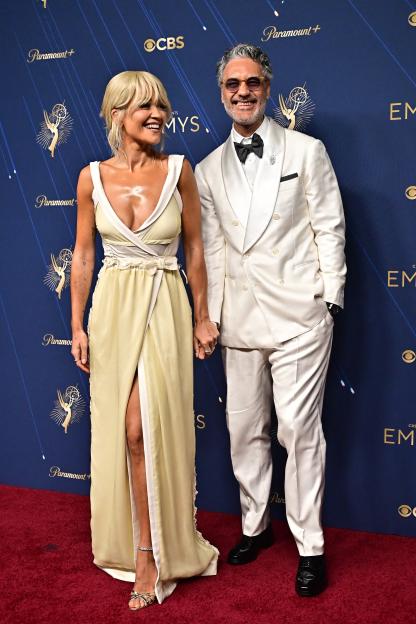 Taika Waititi in a white tuxedo and Rita Ora in a yellow Miu Miu dress at the 77th Primetime Emmy Awards.