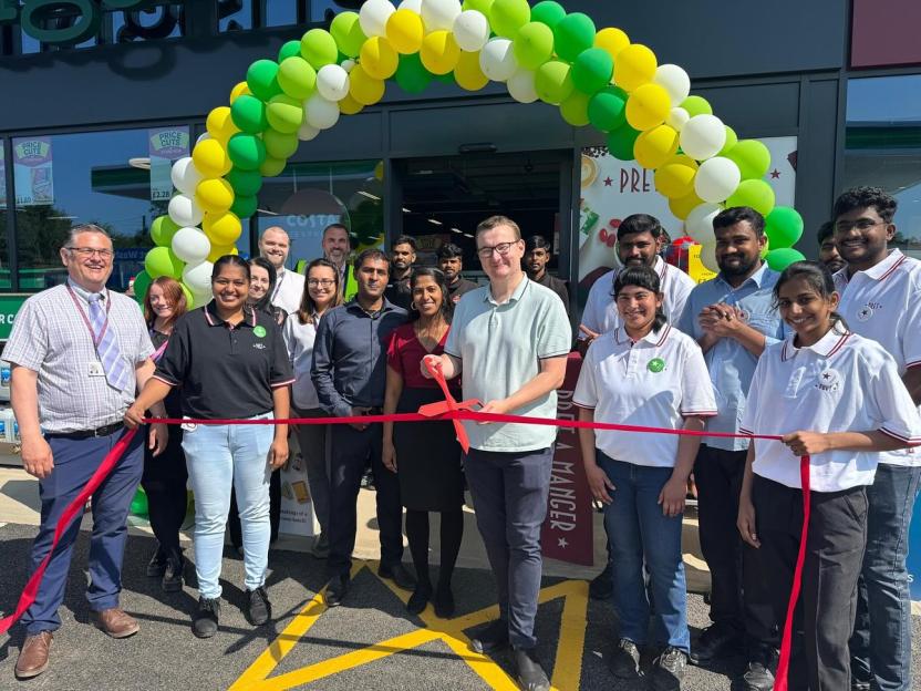 Group of people cutting a red ribbon in front of a new store with a balloon arch.