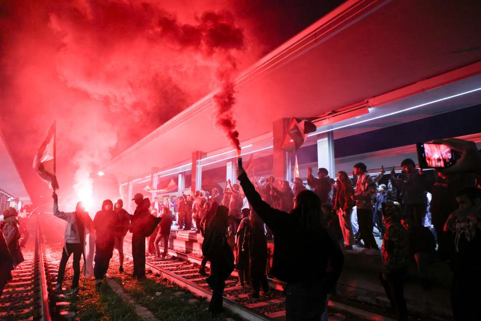 Protesters blocking railway tracks with red smoke and flags.