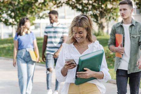 Smiling young woman walking with classmates, using her phone.