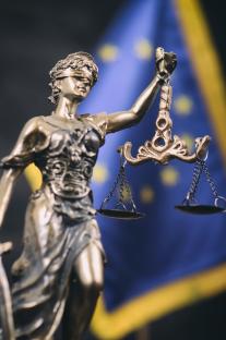 Statue of Lady Justice with scales, in front of the European Union flag.