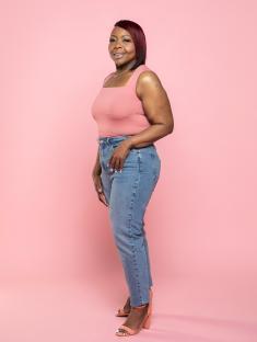 Woman in pink top and jeans smiling against a pink background.