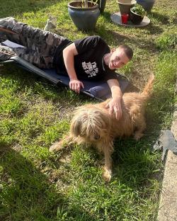 Man petting a dog in a grassy yard.