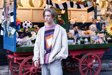 A young man stands in front of a flower-laden cart.