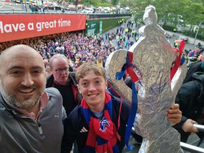 A father and his two sons at a football match, holding a foil replica of the FA Cup trophy.