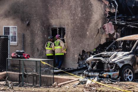Firefighters examining a fire-damaged home and vehicle.
