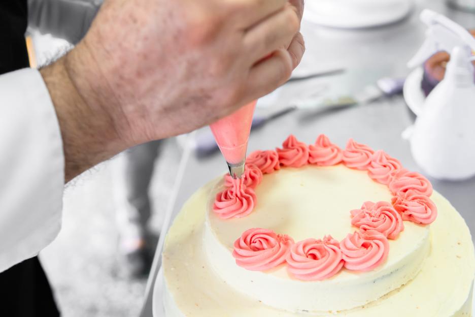 Pastry chef decorating a cake with pink frosting.