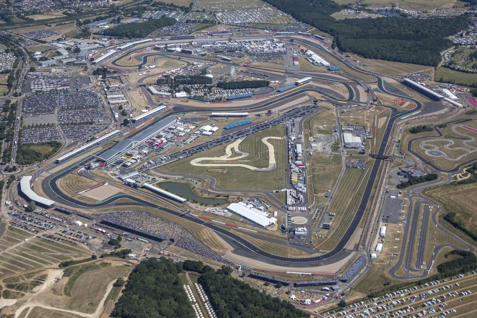 Aerial view of the British Grand Prix race track at Silverstone, surrounded by parking lots and spectator stands.