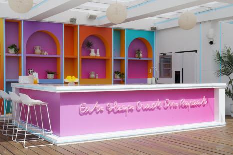 The Love Island villa's kitchen area with a pink bar and neon sign reading