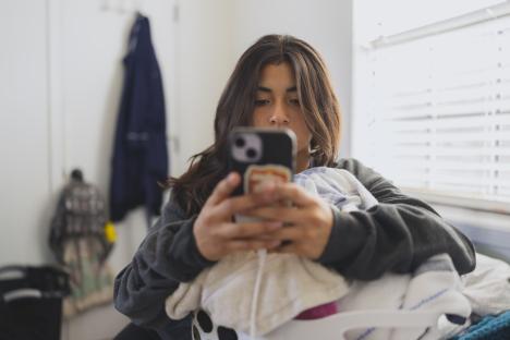 Teenage girl texting on her phone before doing laundry.
