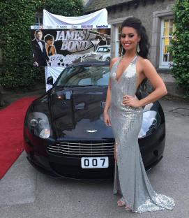 Woman in a sequined gown standing next to a James Bond themed Aston Martin.